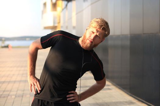 Handsome young man doing stretching exercises before running while standing outdoors