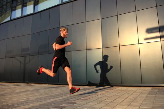 Sporty young man running outdoors to stay healthy, at sunset or sunrise. Runner