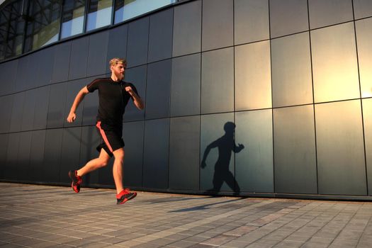 Sporty young man running outdoors to stay healthy, at sunset or sunrise. Runner