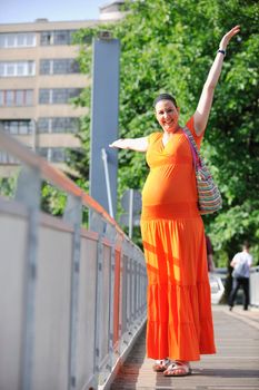 beautiful young happy pregnant woman outdoor in bright nature in orange dress