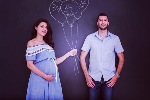 Conceptual photo of pregnant couple drawing their imaginations about the future life with children on chalk board