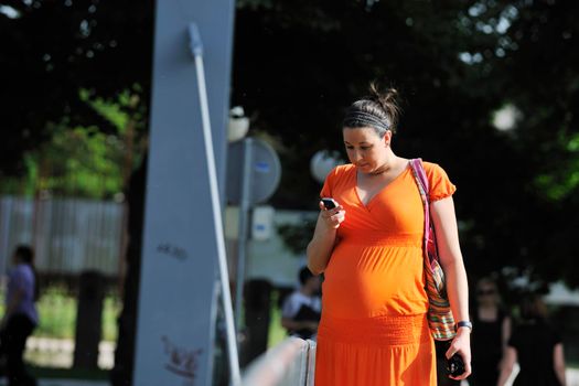 BEAUTIFUL YOUNG PREGNANT WOMAN WALKING OUTDOOR AND TAKING ON CELLPHONE