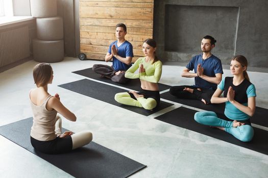 Yoga teacher and beginners in class, making asana exercises. Lotus pose. Healthy lifestyle in fitness club. Stretching with coach