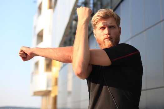 Handsome young man doing stretching exercises before running while standing outdoors