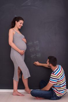 young pregnant couple accounts week of pregnancy and writing them with chalk on blackboard