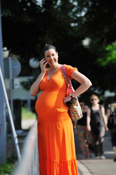 BEAUTIFUL YOUNG PREGNANT WOMAN WALKING OUTDOOR AND TAKING ON CELLPHONE