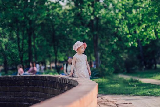 young mother with a little daughter standing near the city fountain on a hot summer day