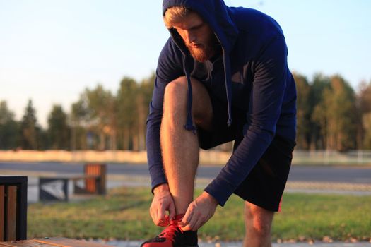 Fit athlete. Handsome adult man runner tying shoelaces at sunset or sunrise.