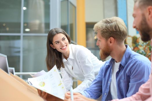 Group of young people in casual wear sitting at the office desk and discussing something while looking at PC together