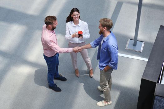 Top view of young modern people in smart casual wear shaking hands standing with their colleagues in creative office