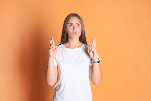 Young woman in basic clothing with fingers crossed isolated over yellow background