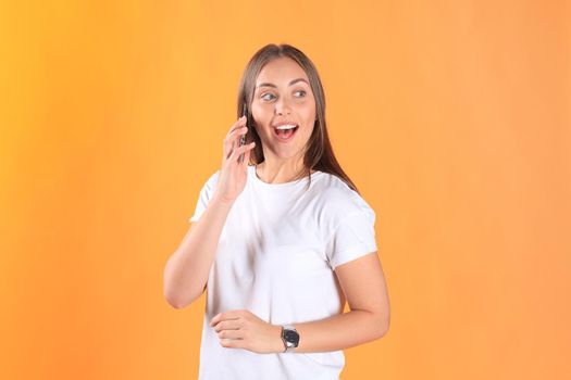 Young woman dressed in basic clothing isolated on yellow background, talking on mobile phone.