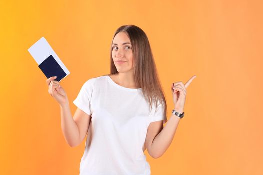 Excited young woman tourist standing isolated on yellow background holding passport with tickets, plastic credit card.