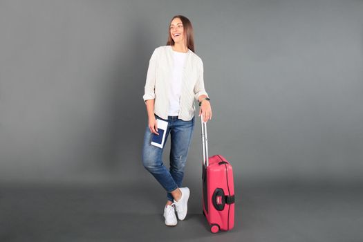 Young tourist girl in summer casual clothes, with sunglasses, red suitcase, passport, tickets isolated grey background.