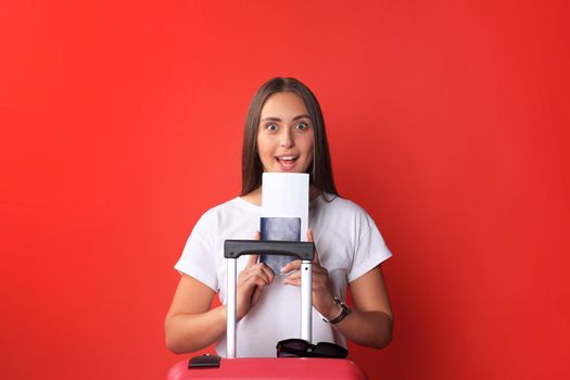 Young tourist girl in summer casual clothes, with sunglasses, red suitcase, passport isolated on red background.