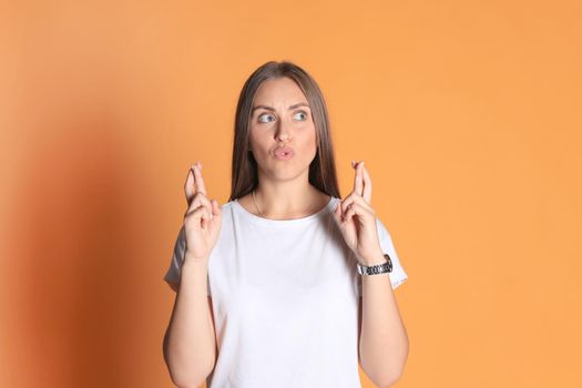 Young woman in basic clothing with fingers crossed isolated over yellow background