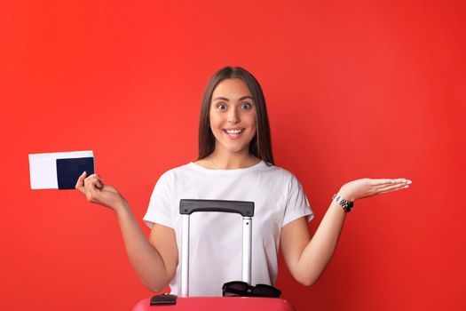 Young tourist girl in summer casual clothes, with sunglasses, red suitcase, passport isolated on red background.