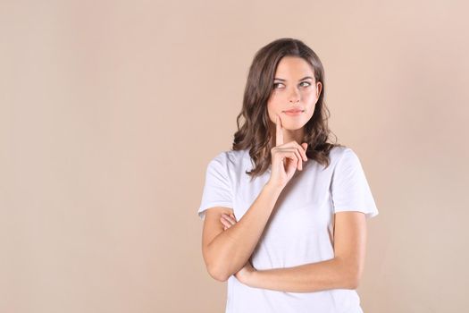 Cheerful brunette woman dressed in basic clothing looking at camera, isolated on beige background