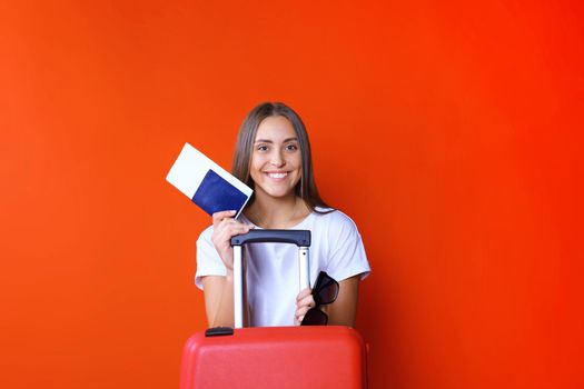 Young tourist girl in summer casual clothes, with sunglasses, red suitcase, passport isolated on red background.