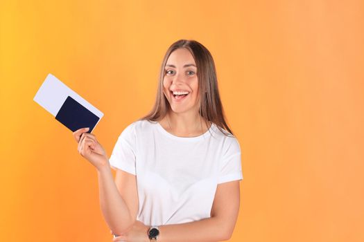 Excited young woman tourist standing isolated on yellow background holding passport with tickets, plastic credit card.