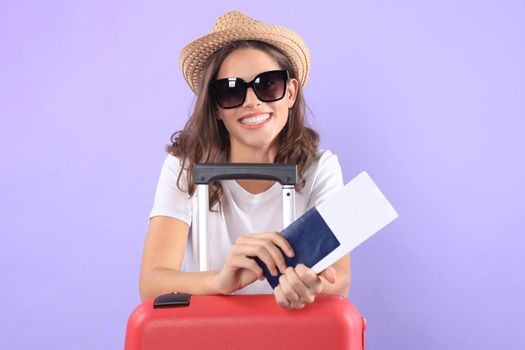 Young tourist girl in summer casual clothes, with sunglasses, red suitcase, passport isolated on purple background