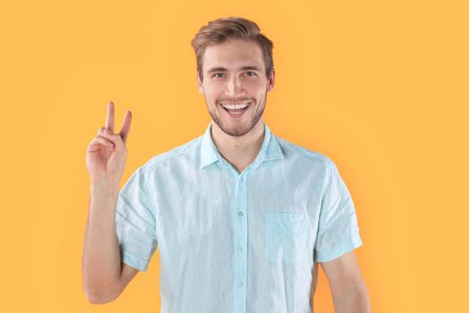 Young man showing peace sign isolated over yellow background