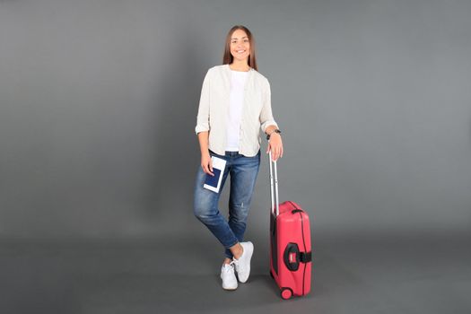 Young tourist girl in summer casual clothes, with sunglasses, red suitcase, passport, tickets isolated grey background.