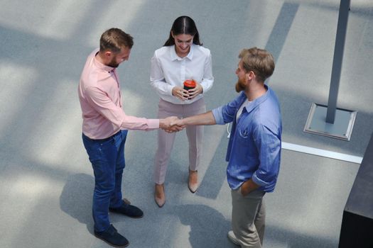 Top view of young modern people in smart casual wear shaking hands standing with their colleagues in creative office