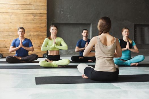 Yoga teacher and beginners in class, making asana exercises. Lotus pose. Healthy lifestyle in fitness club. Stretching with coach