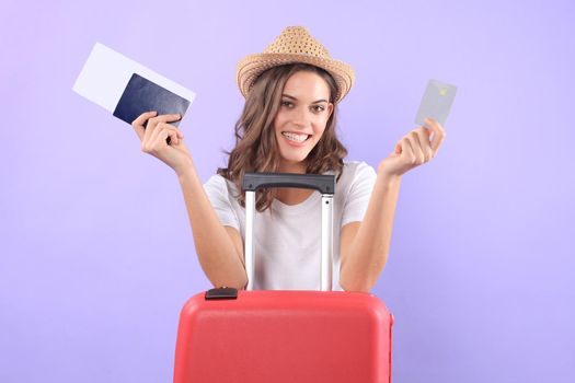 Young tourist girl in summer casual clothes, with sunglasses, red suitcase, passport isolated on purple background