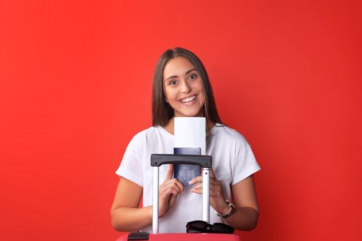 Young tourist girl in summer casual clothes, with sunglasses, red suitcase, passport isolated on red background.