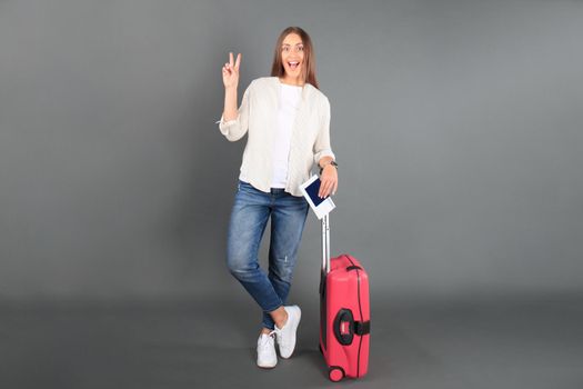 Young tourist girl in summer casual clothes, with sunglasses, red suitcase, passport, tickets isolated grey background.