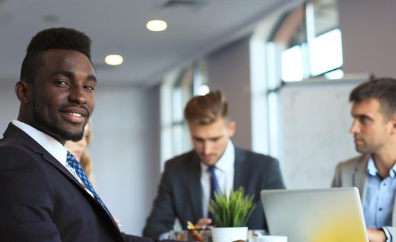 Smiling confident African businessman in a meeting with a colleagues seated at a conference table in the office.