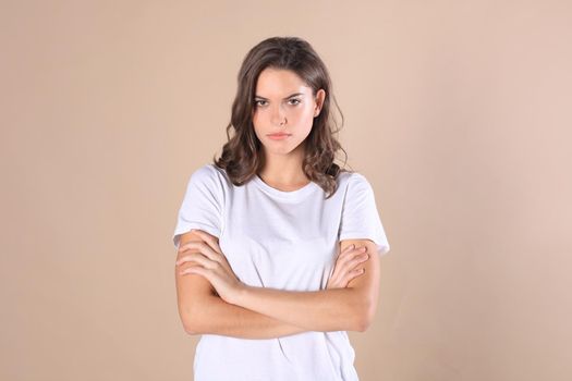 Cheerful brunette woman dressed in basic clothing looking at camera, isolated on beige background