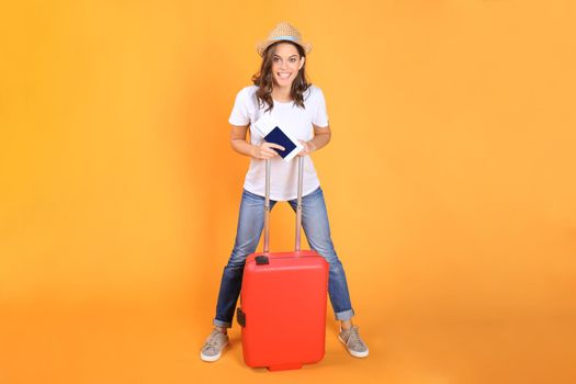 Young tourist girl in summer casual clothes, with red suitcase, passport, tickets isolated on beige background