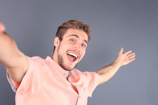 Young man isolated over gray backgound, taking a selfie