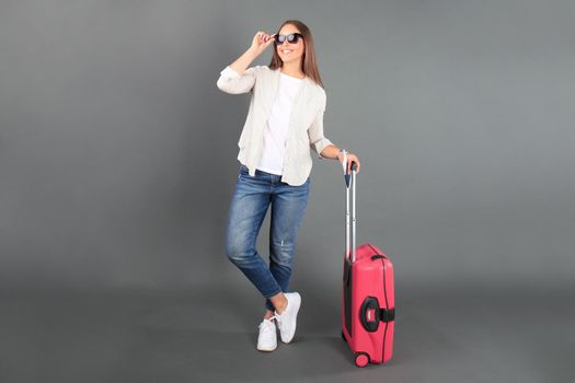 Young tourist girl in summer casual clothes, with sunglasses, red suitcase, passport, tickets isolated grey background.