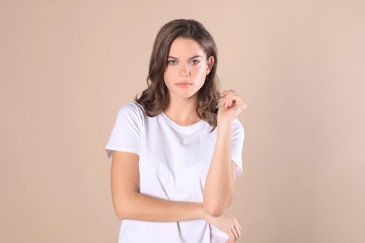 Cheerful brunette woman dressed in basic clothing looking at camera, isolated on beige background