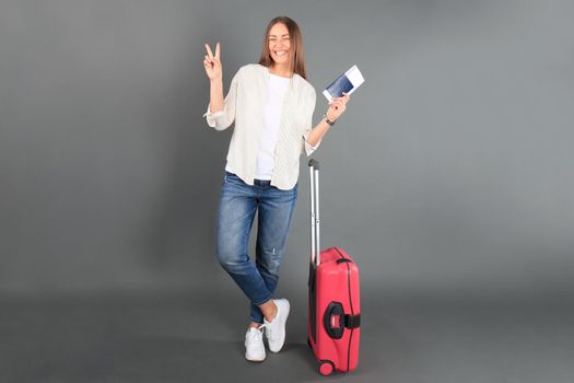 Young tourist girl in summer casual clothes, with sunglasses, red suitcase, passport, tickets isolated grey background.