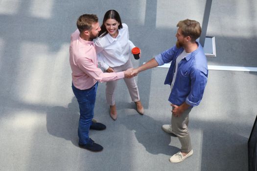 Top view of young modern people in smart casual wear shaking hands standing with their colleagues in creative office