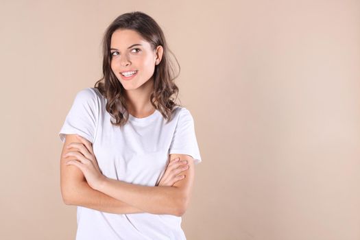 Cheerful brunette woman dressed in basic clothing looking at camera, isolated on beige background