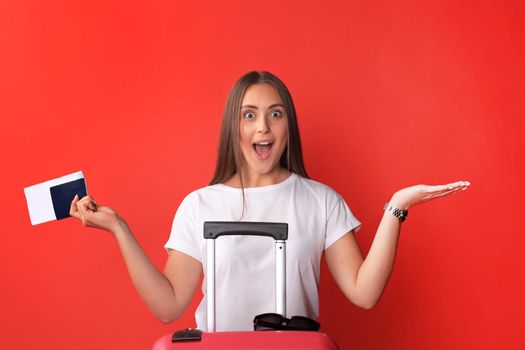 Young tourist girl in summer casual clothes, with sunglasses, red suitcase, passport isolated on red background.