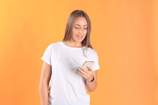 Young woman dressed in basic clothing isolated on yellow background, using mobile phone.