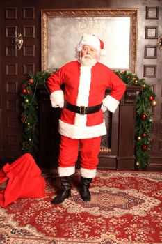 Traditional Santa Claus standing by the fireplace and Christmas tree in a room.