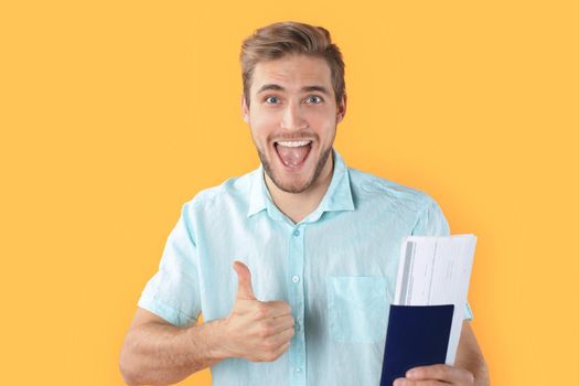 Young man isolated over yellow background holding passport pointing