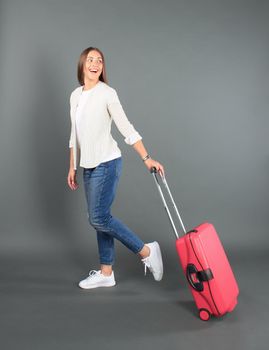 Young tourist girl in summer casual clothes, with sunglasses, red suitcase, passport, tickets isolated grey background.