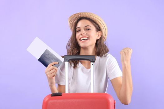 Young tourist girl in summer casual clothes, with sunglasses, red suitcase, passport isolated on purple background