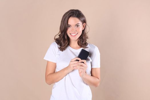 Young woman dressed in basic clothing isolated on beige background, using mobile phone