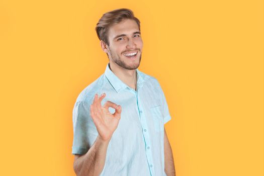Young man showing ok isolated over yellow background