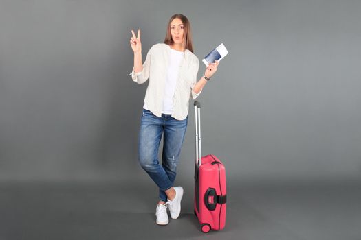 Young tourist girl in summer casual clothes, with sunglasses, red suitcase, passport, tickets isolated grey background.